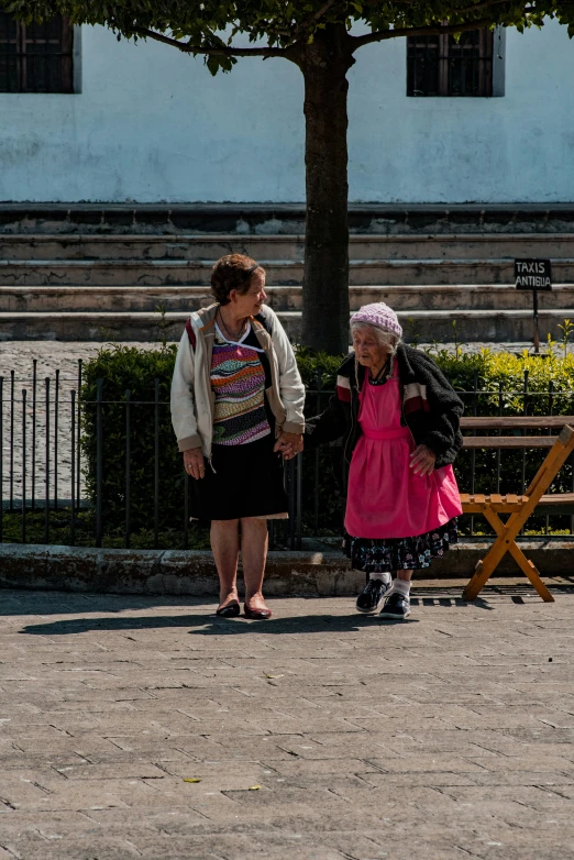 a woman standing next to a little girl who is sitting on a bench