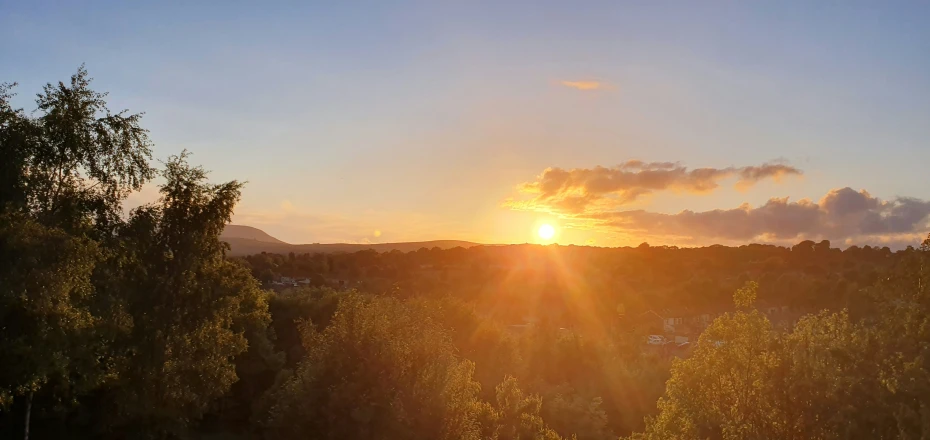 the sun setting in between two hills covered in trees