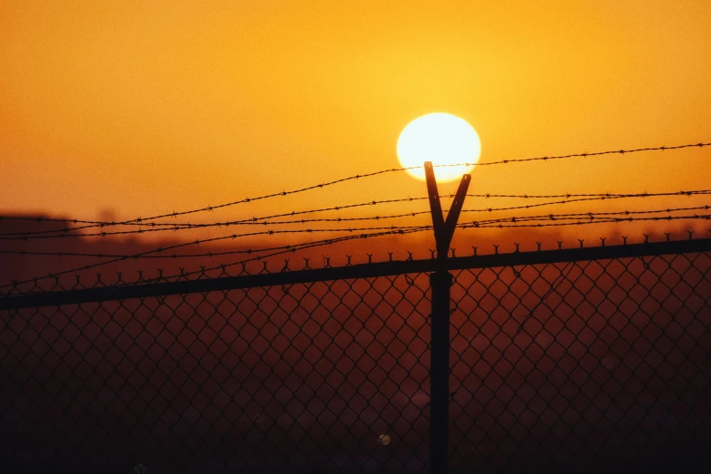 a sunset over a fence with a line of wire in the foreground