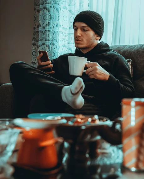 man in black outfit sitting with his legs crossed drinking coffee