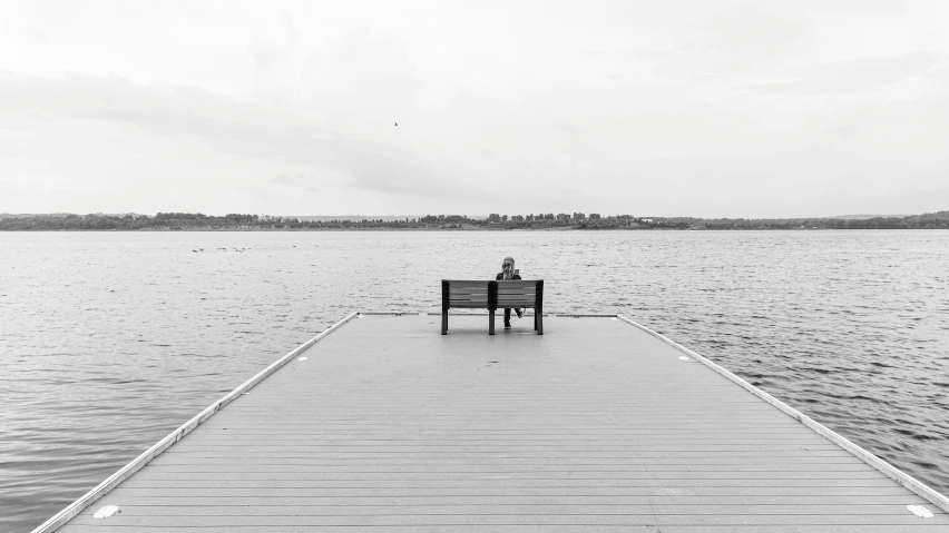 there is a man sitting on a bench on the pier