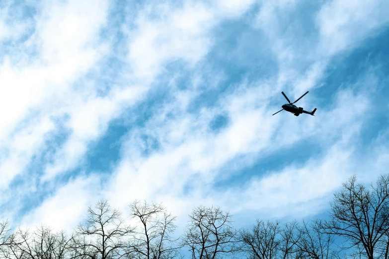 a helicopter flies over trees and blue sky