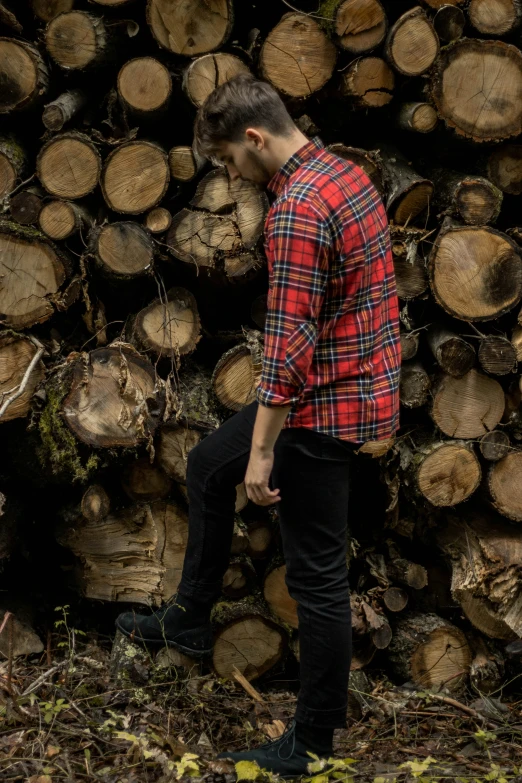 a young man is walking in front of a stack of cut wood