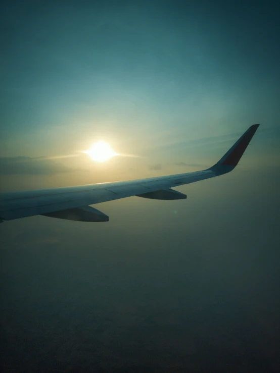 an airplane wing flies through the sky as the sun sets