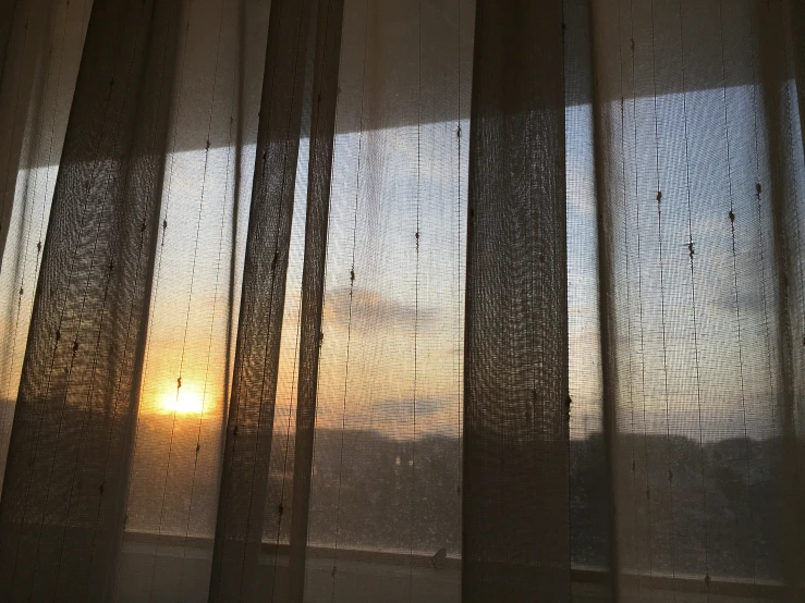 the sun rises through a sheer curtained window