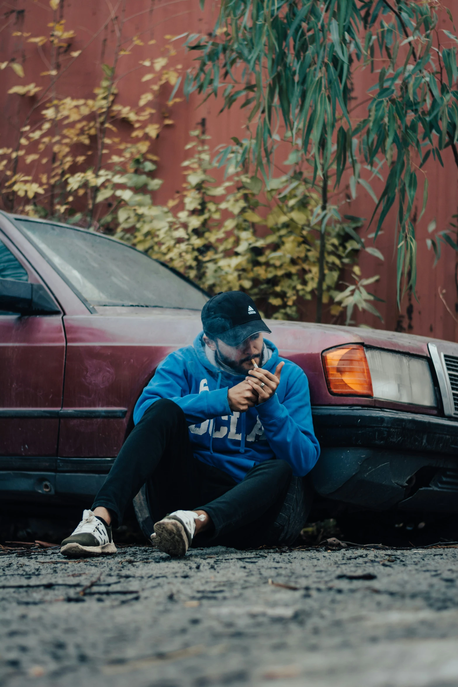 a man sitting in the street next to a parked red car