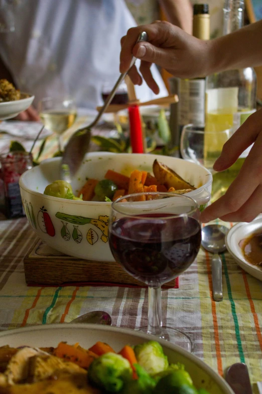 some people on a table with plates of food and a glass of wine