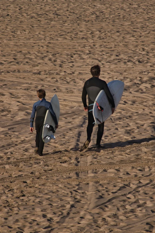 two men holding their surf boards walking in the sand