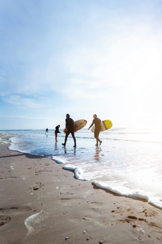 three surfers walk along the beach towards the ocean