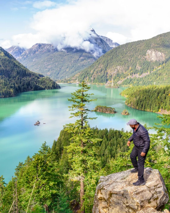 a man standing on top of a rocky cliff in front of lake