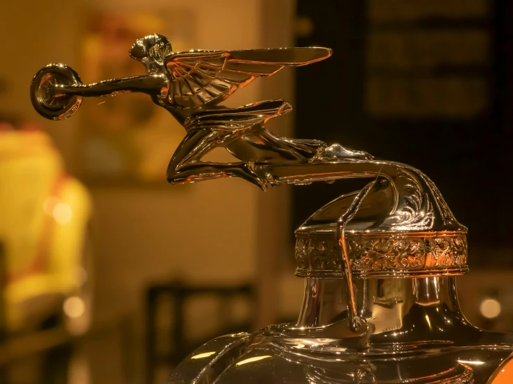 a golden hood ornament that looks like a figure riding on top of a shiny chrome car