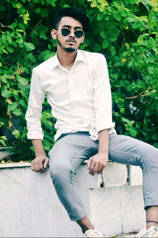 man in a white shirt and sunglasses sitting on a wall