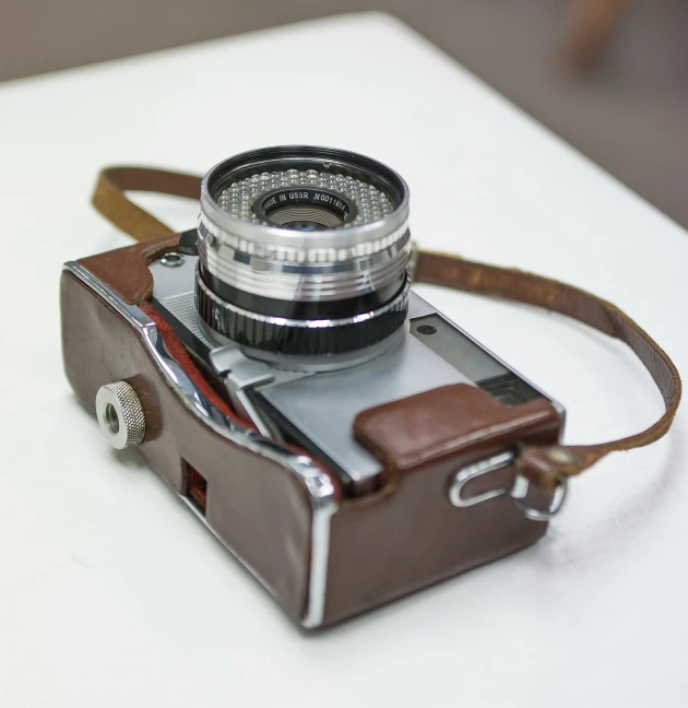 the small camera has a leather strap around the lens