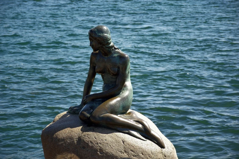 a statue sitting on top of a rock next to the water