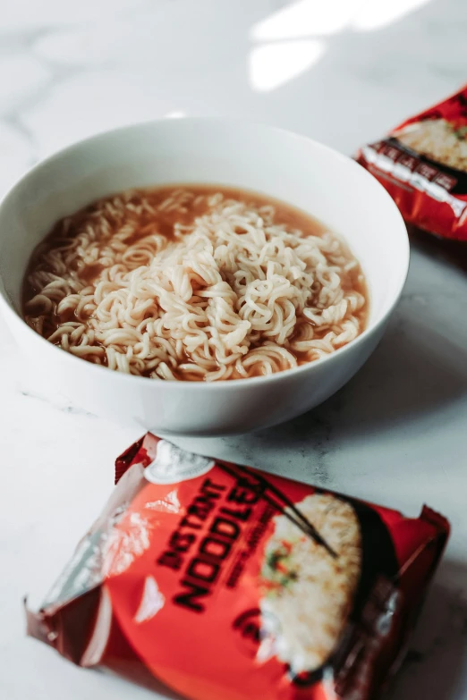 two bowls filled with noodle soup next to bagged noodles