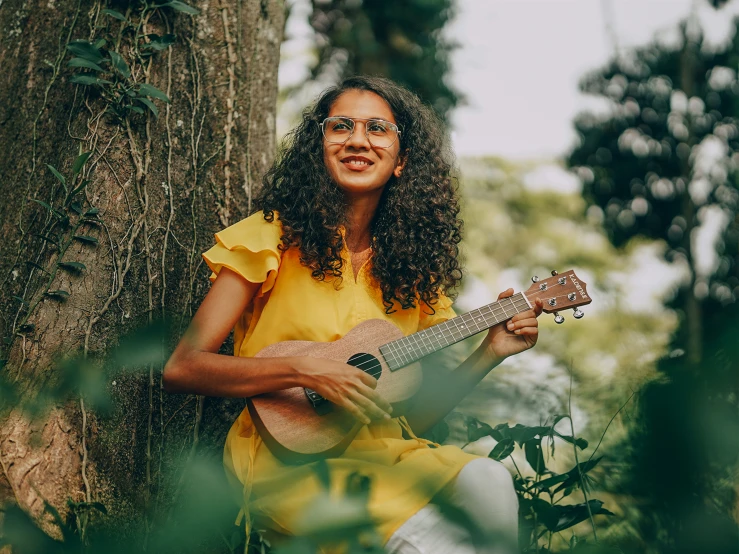 a woman holding a ukelet sitting under a tree