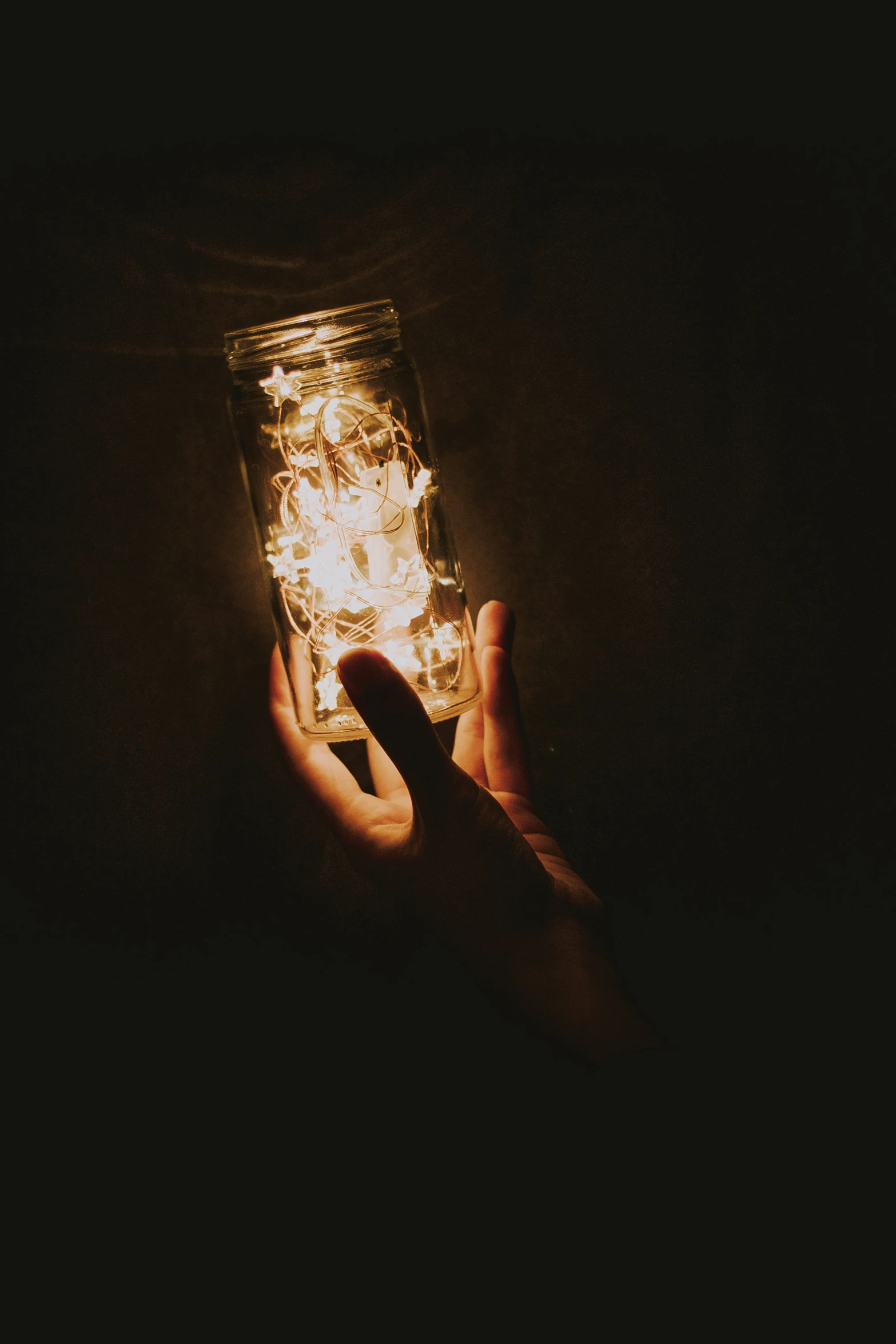 a hand holds a glowing lit glass jar in the dark