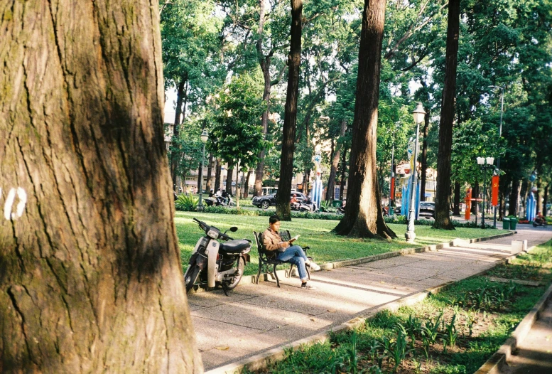 a man sits in the park next to a scooter