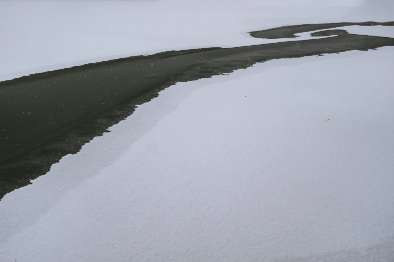 snowy field with black patches on it and a road