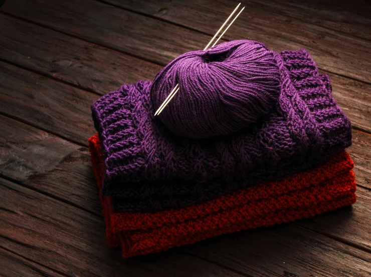 knitting needles are laying on sweaters and hat
