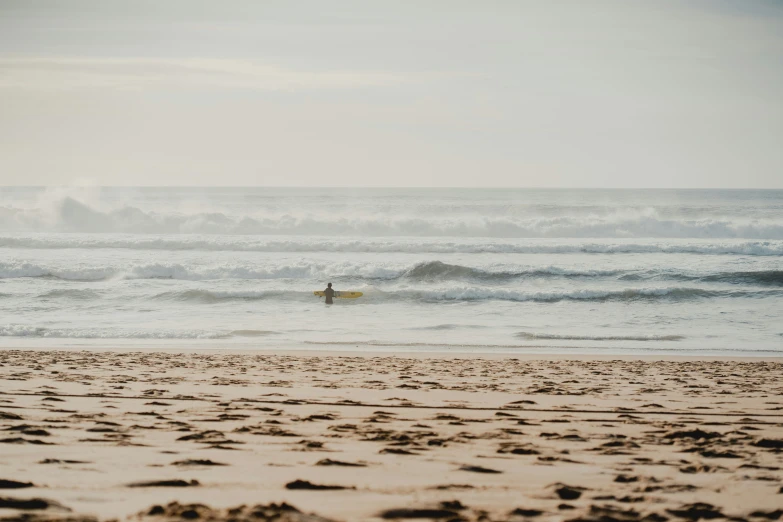 a person holding a surf board walking across the beach