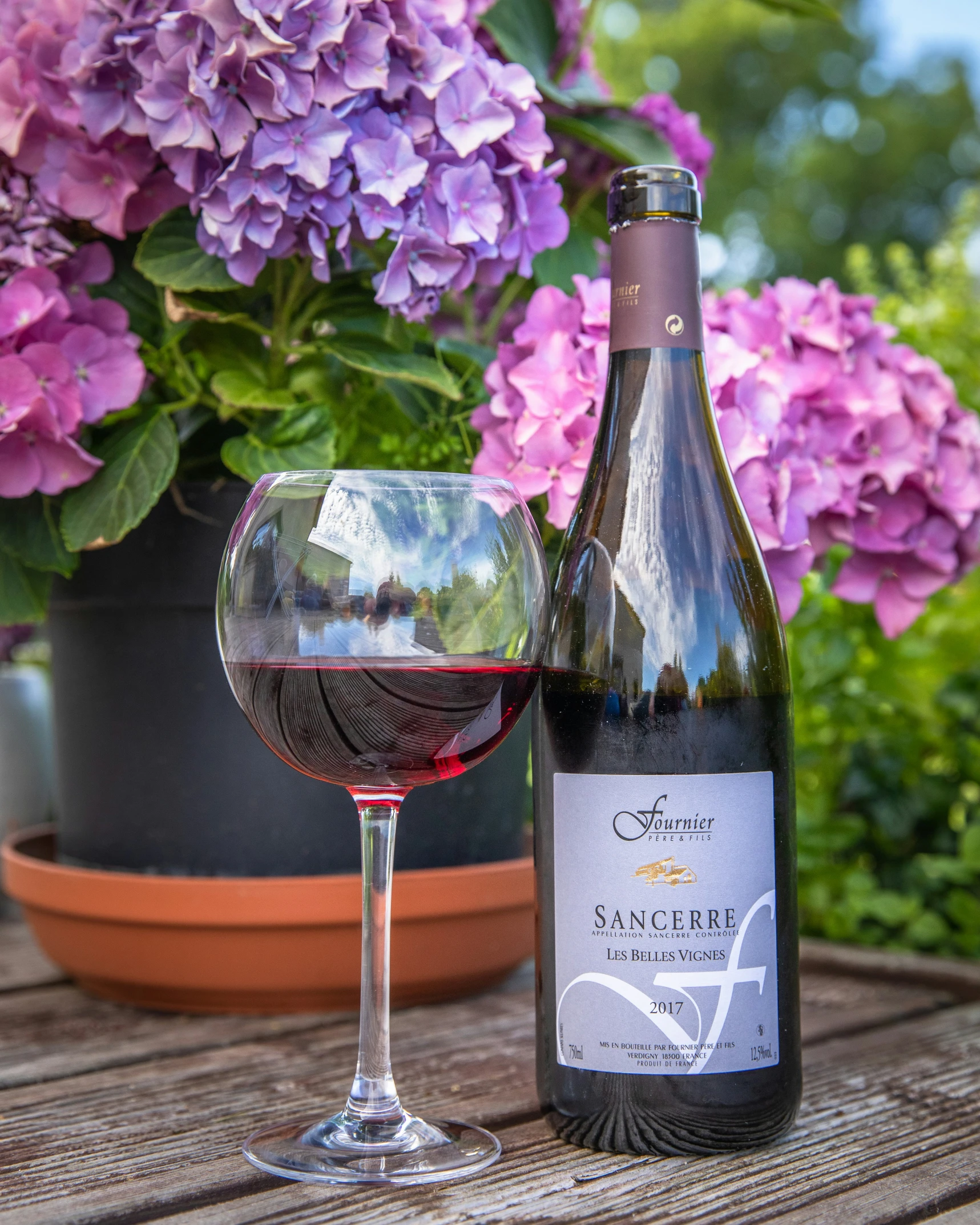 a bottle and wine glass sitting on a table outside with pink flowers