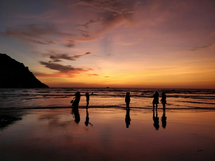 silhouettes of people standing on the beach at sunset