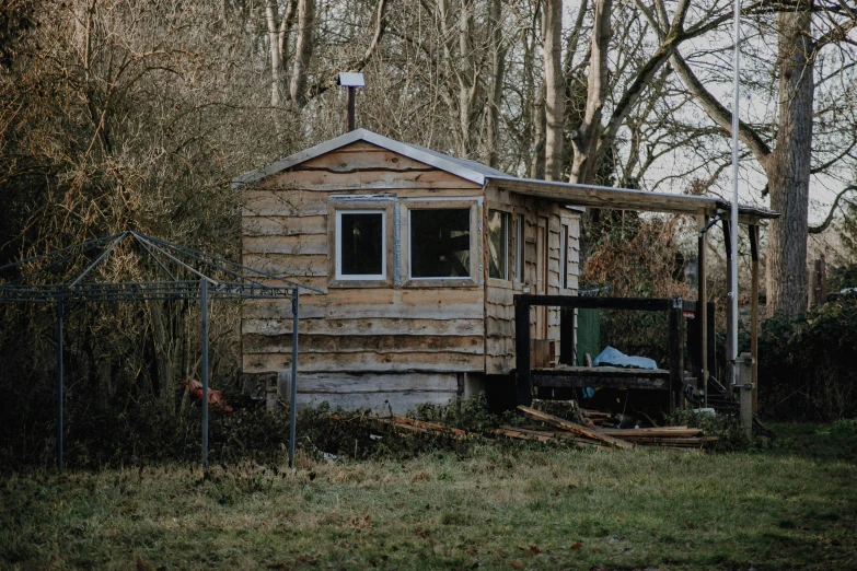 a small wood building in a field with fence and trees