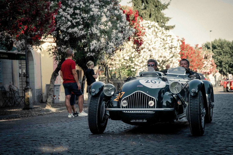 two men ride in an antique vehicle down the road