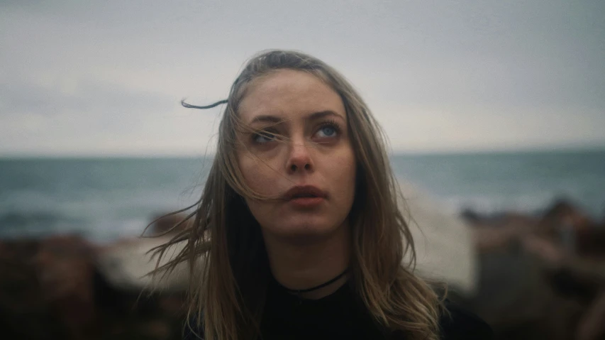 a woman looks directly into the camera while people sit around on the beach