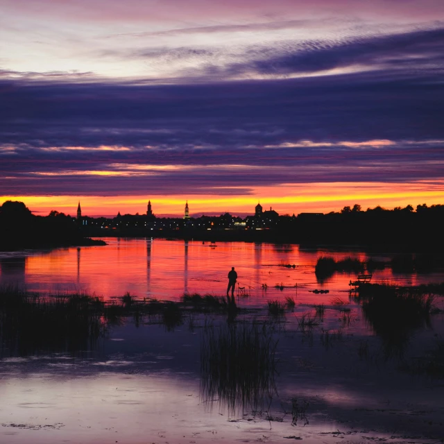 a man stands on the edge of a body of water as the sun sets