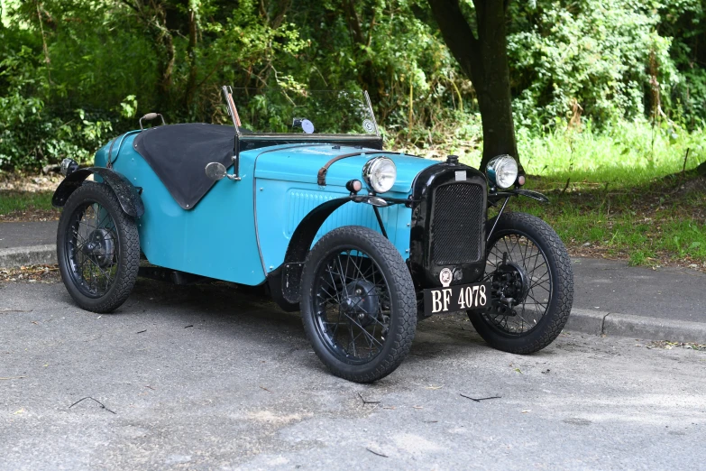 a blue antique car on the road in front of some trees