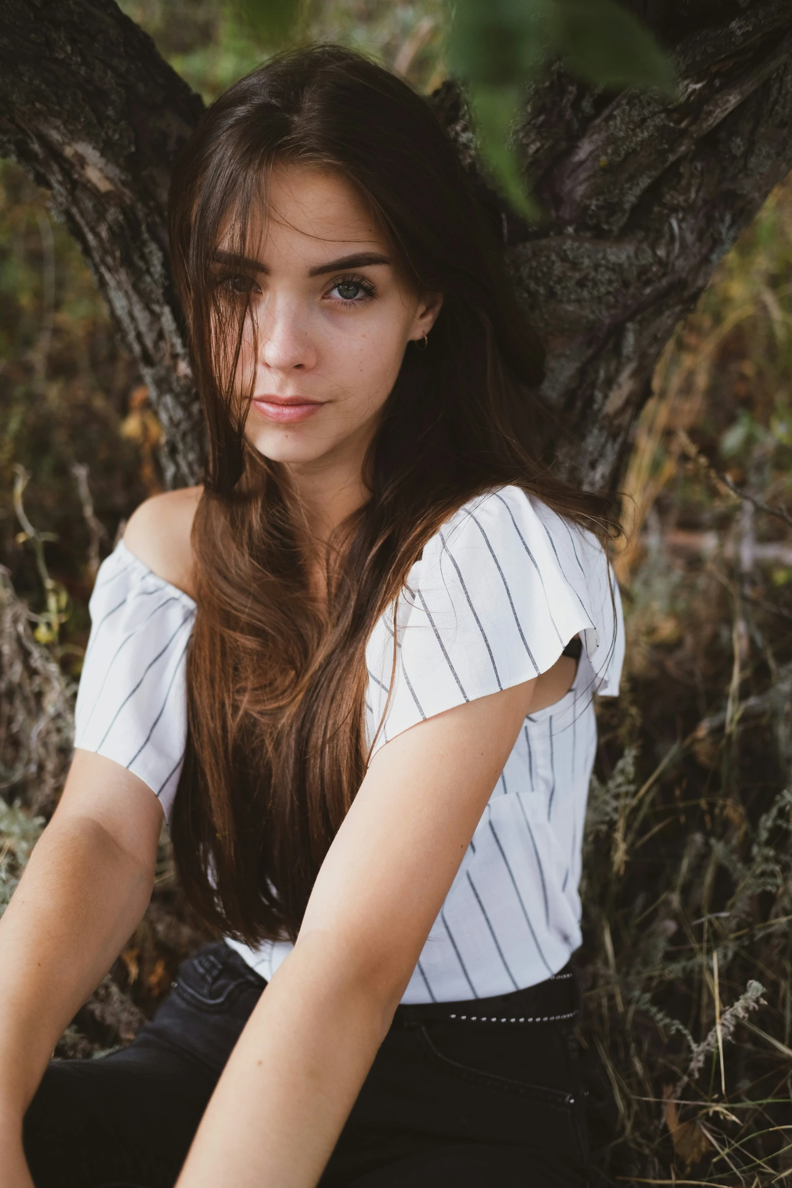 a girl posing against a tree and wearing a white top