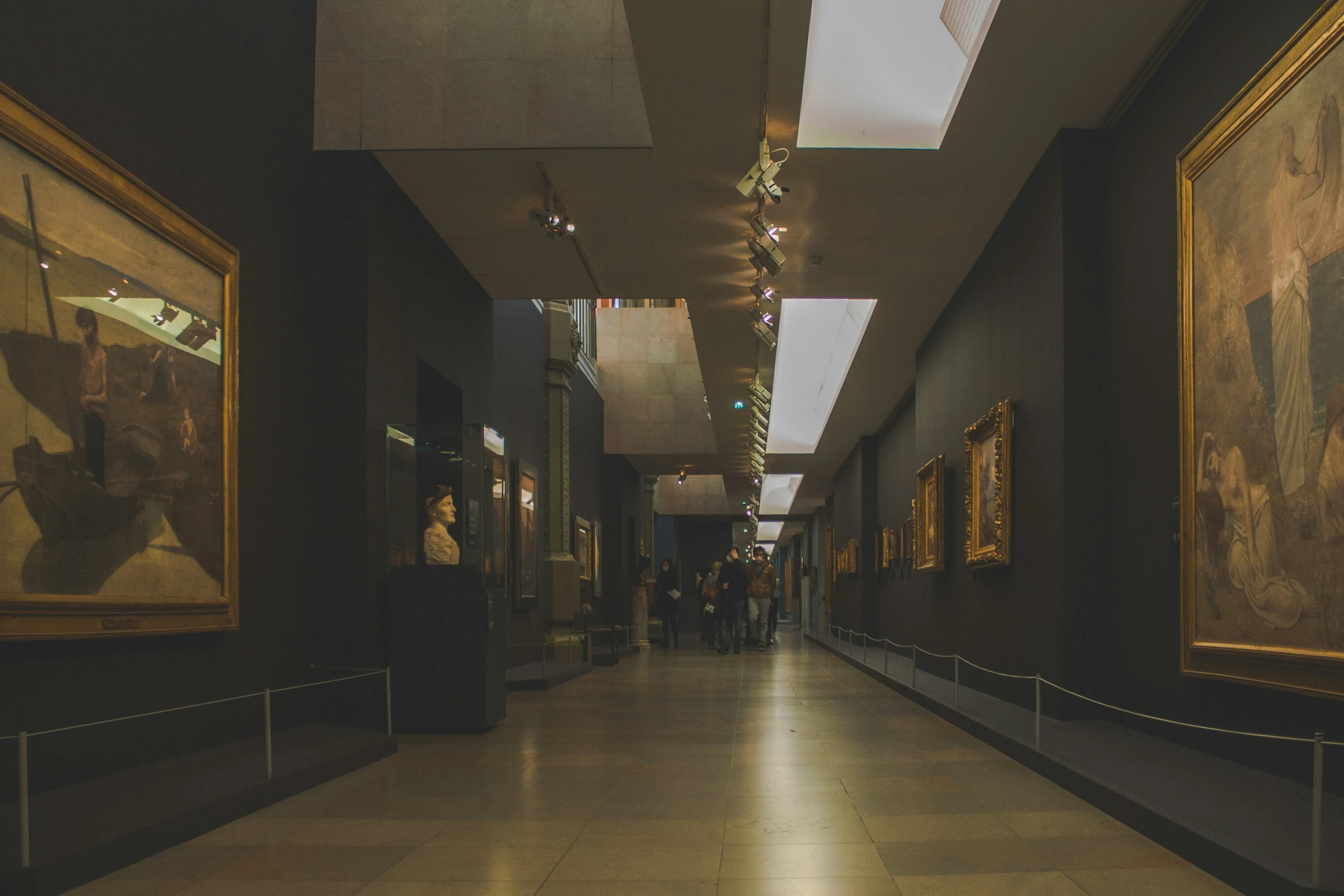 people walking through the hall in front of two paintings