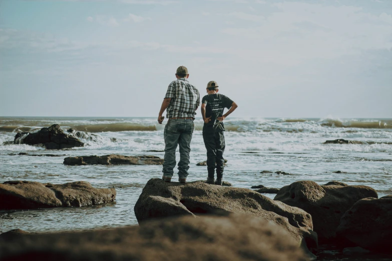 a pair of men standing on top of a rocky beach