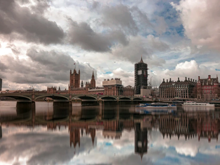 the clouds are overcastting buildings, and a boat is docked in the water