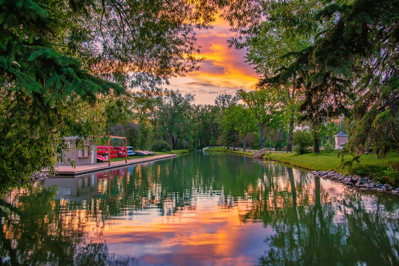 sunset over the water between a tree lined bank and dock