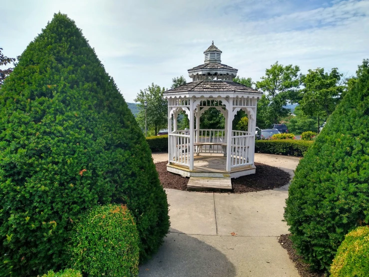 a small white gazebo sitting among some hedges