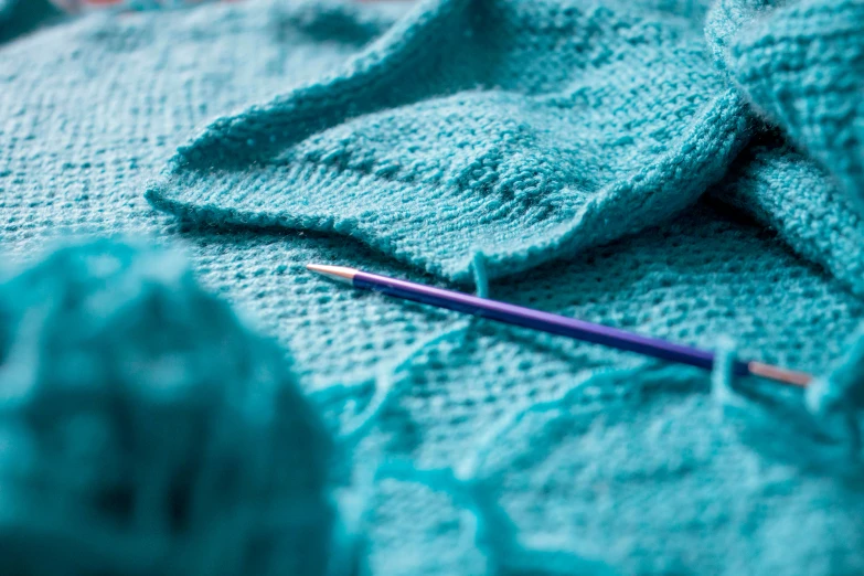 a knitting machine with blue yarn next to knitted blanket