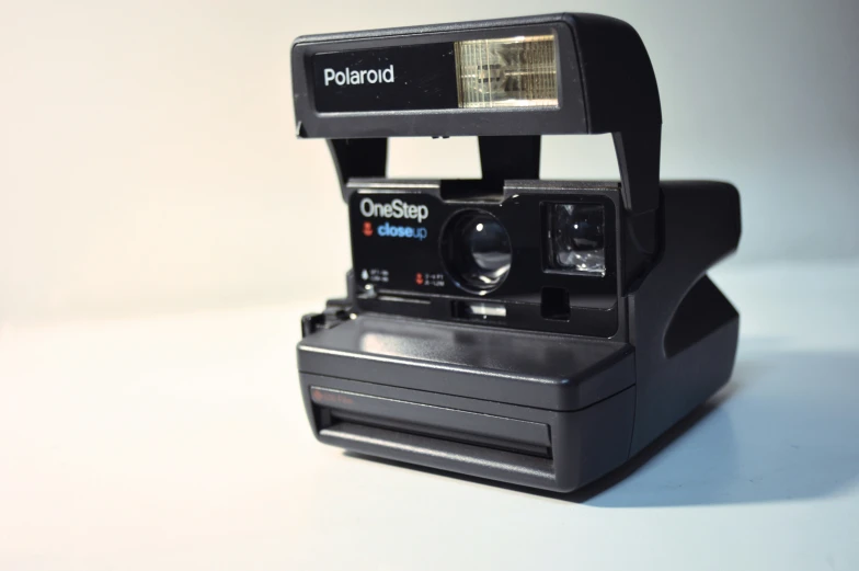 a polaroid camera, with a flash light and some small objects in front of it