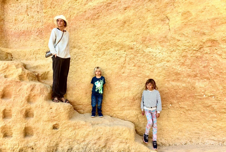 a woman and two children standing on top of some sand