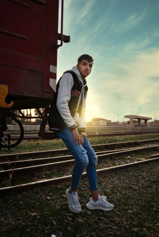 a guy sitting on a rail in front of train tracks