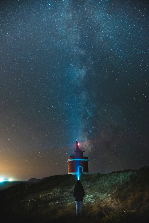 a man standing in the distance under the night sky looking at the stars