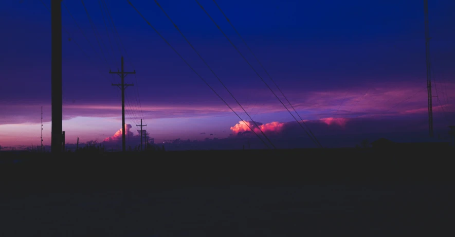 a sunset over telephone poles with purple skies in the background