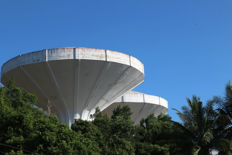 three white concrete structures surrounded by trees and blue sky