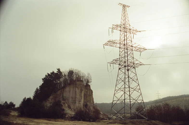 an overhead power pole near a hill under cloudy skies