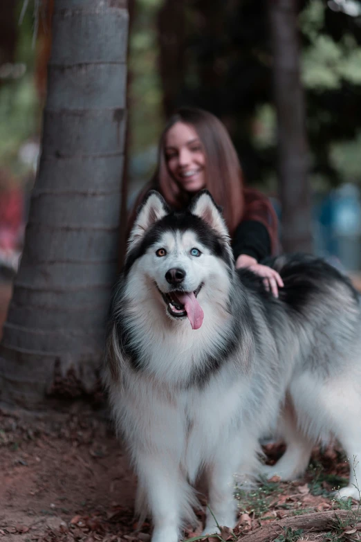 a woman poses in front of a husky dog