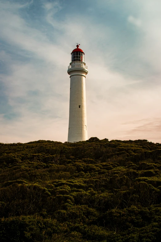 there is a tall white and red light house on top of a hill