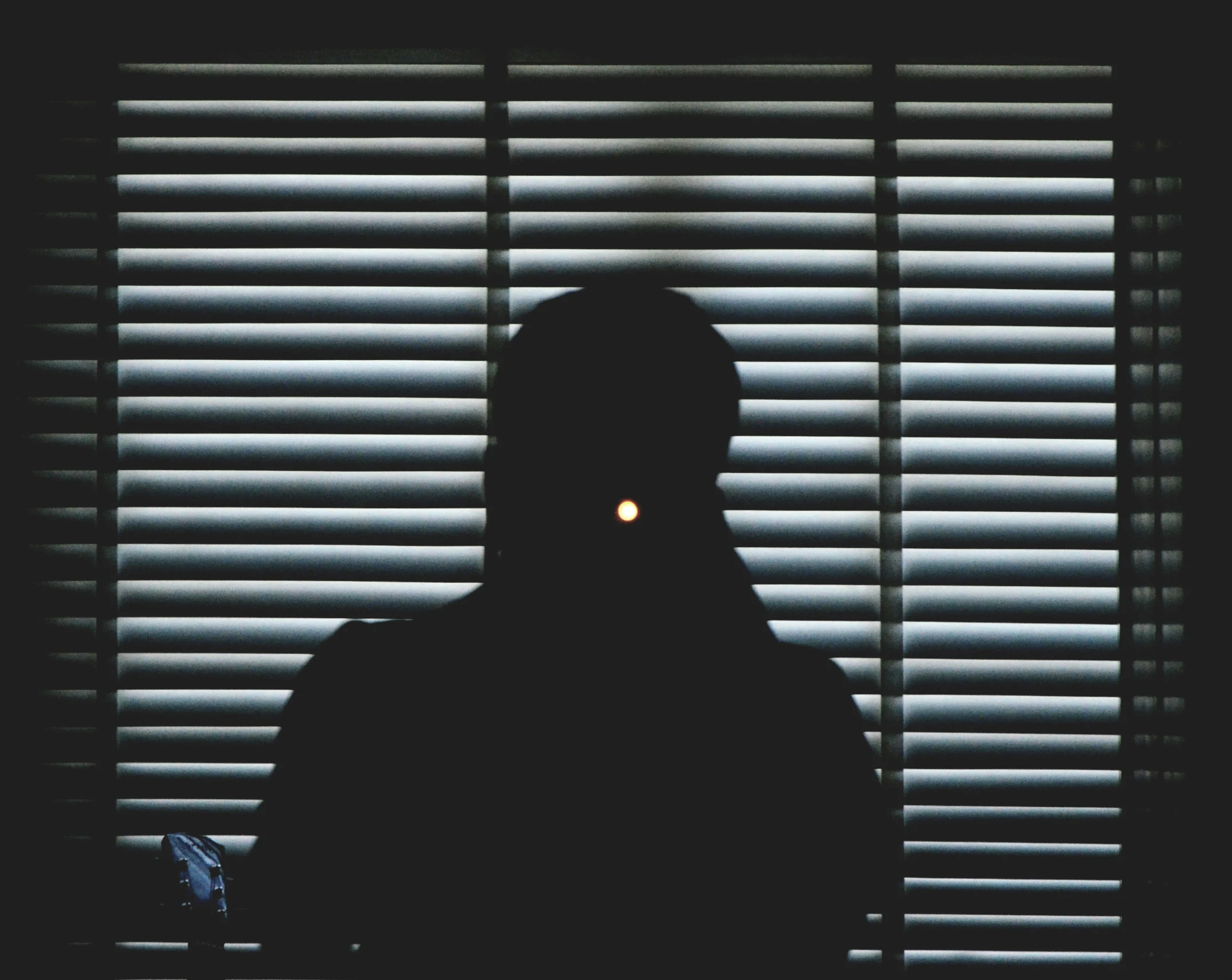 a person is in silhouette, with blinds lit on