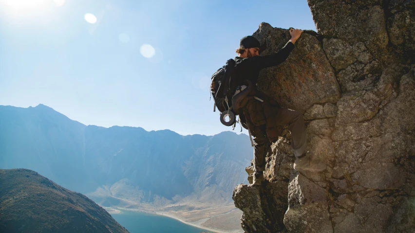 man climbing a large rocky mountain against a clear blue sky